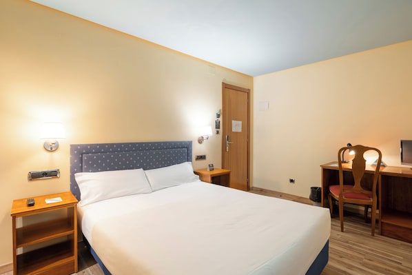 Una habitación de hotel con cama, mesitas de noche, escritorio y silla.
