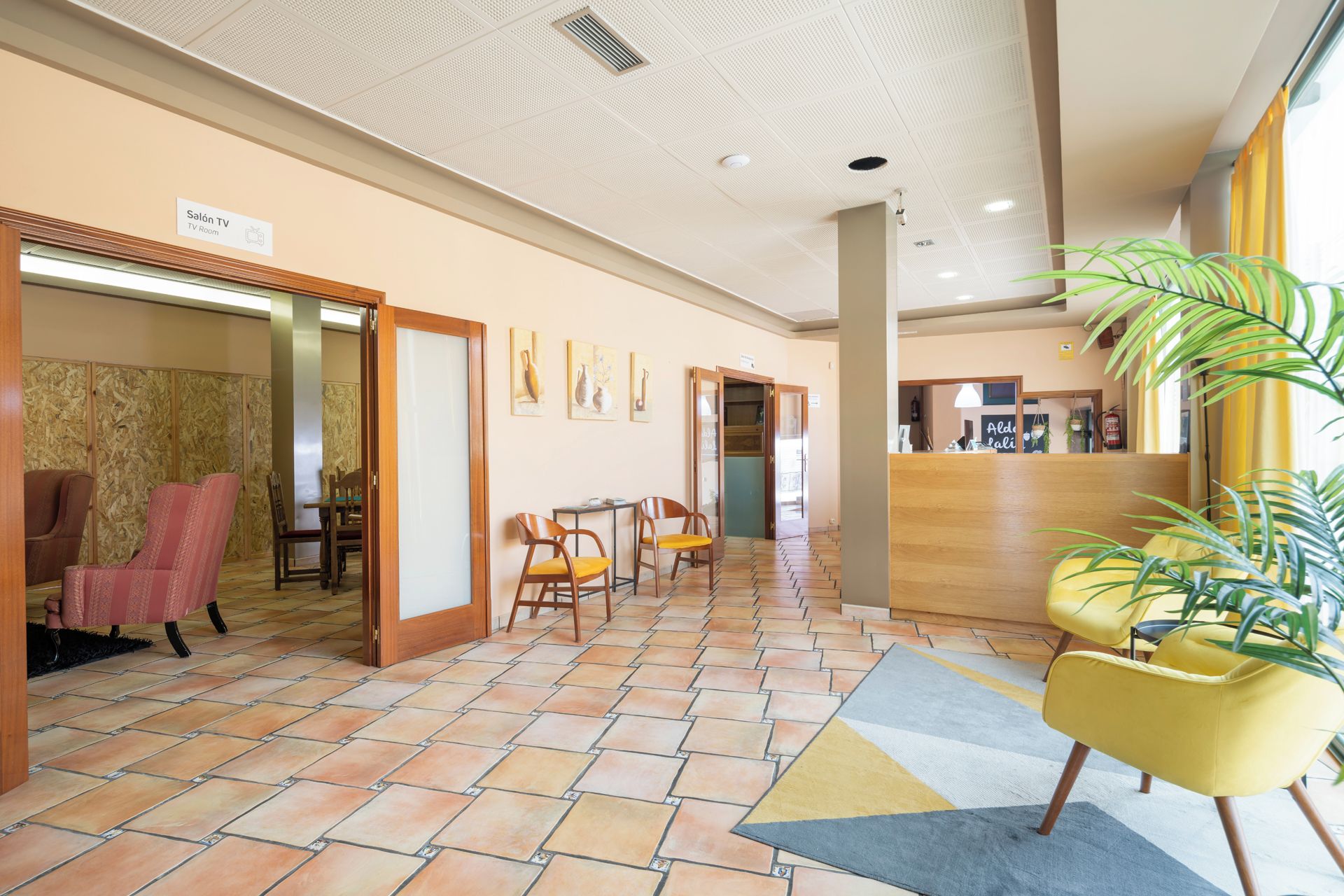 Un vestíbulo de hotel con sala de televisión, zona de estar y mostrador de recepción.