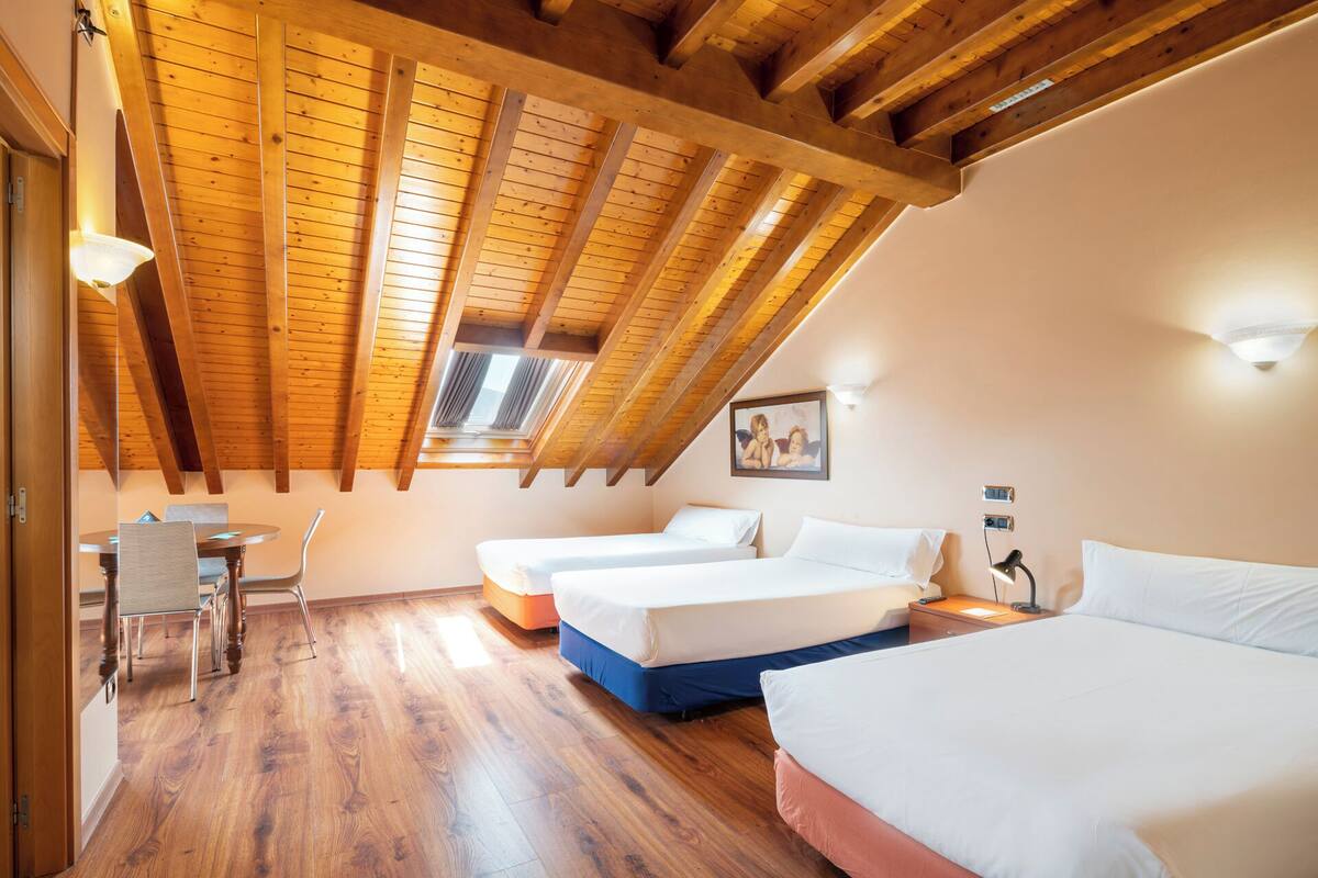 Una habitación con vigas de madera, una mesa de comedor con sillas y tres camas.