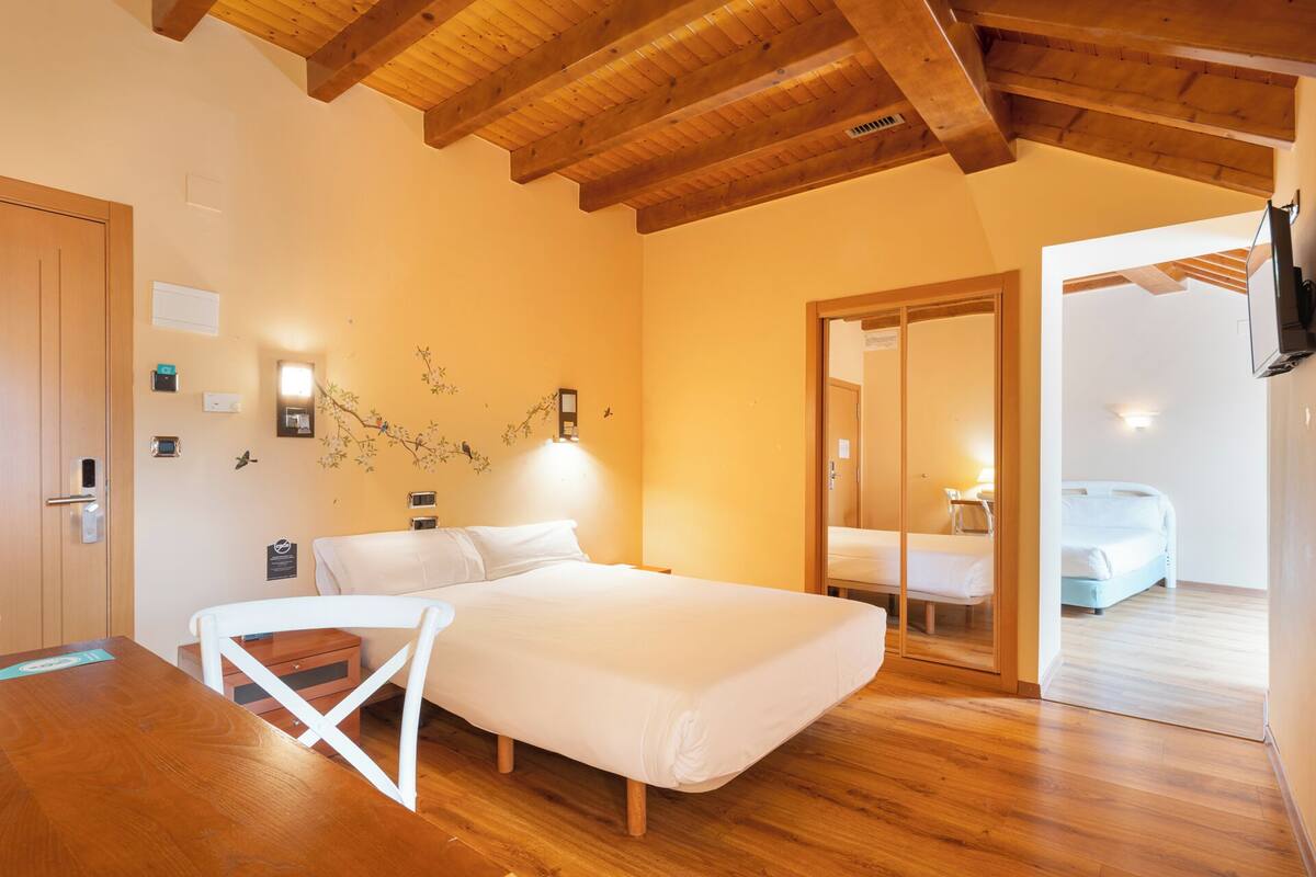 Un dormitorio con techo de madera, una cama, una silla y una mesita.