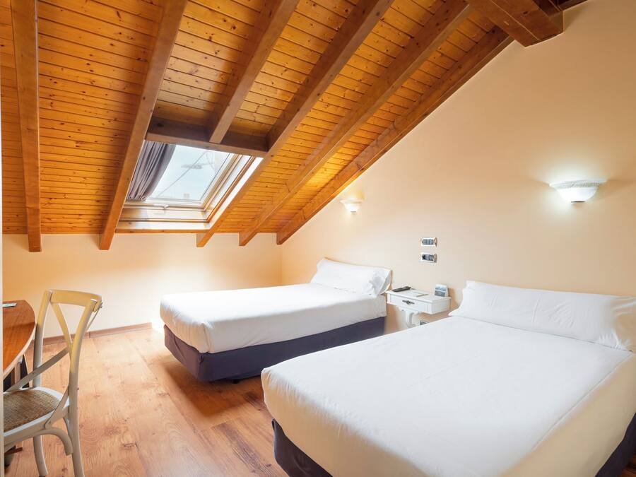 A bedroom with two beds, a wooden ceiling, and a skylight.
