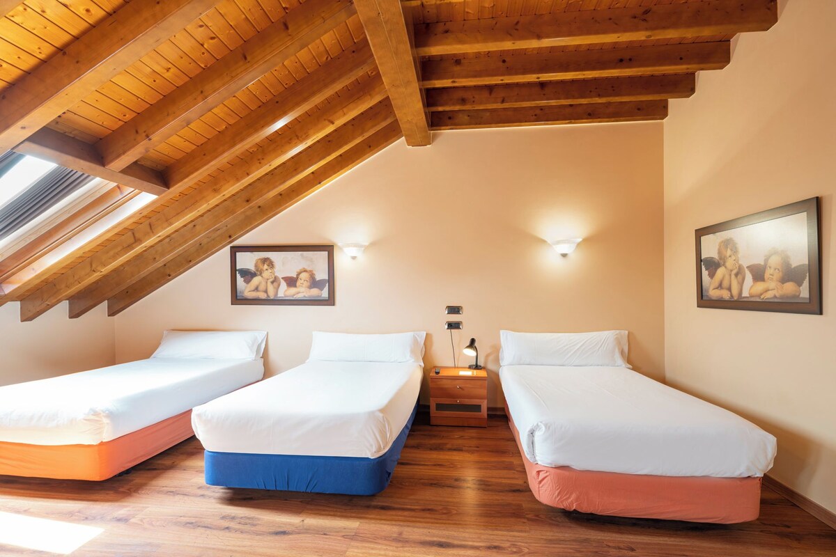 A room with three single beds, wooden ceiling beams, and two wall-mounted light fixtures.
