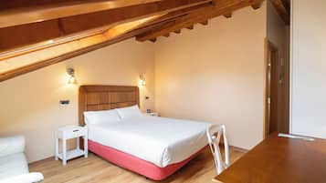 Un dormitorio con techo de madera, cama con ropa de cama blanca, una mesita de noche y un escritorio de madera.