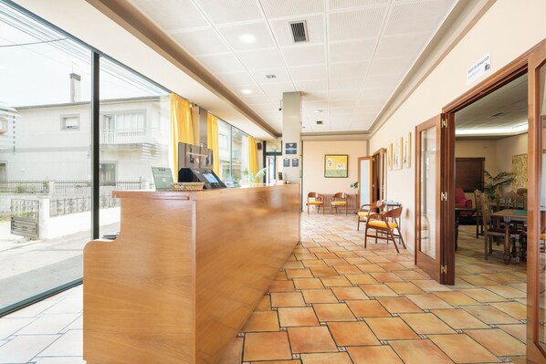 Zona de recepción de un hotel con un mostrador de madera, suelo de baldosas y vistas a la calle.