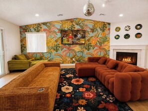 A living room with a sofa, a coffee table, a fireplace, and a wall with a floral mural.