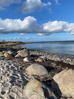 Une plage rocheuse parsemée de gros blocs de pierre, un ciel dégagé et une mer calme.