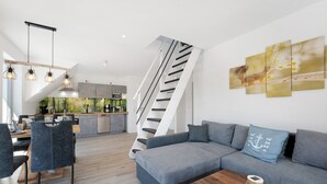 A modern interior with a staircase, grey sofa, dining area, and kitchen.