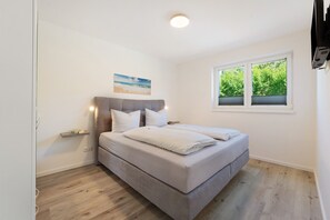 A bedroom with a bed, a window, a painting, and a TV mounted on the wall. - Apartment 'Ostseerauschen - Blaue Welle' with Private Terrace and Wi-Fi (Hohwacht (Ostsee))