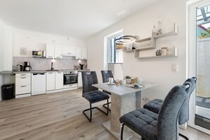 A modern kitchen with white cabinets, a dining area with a central island, and a view of the outdoors. - Apartment 'Ostseerauschen - Blaue Welle' with Private Terrace and Wi-Fi (Hohwacht (Ostsee))