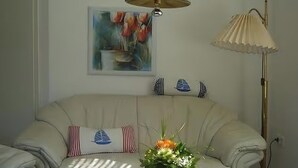 Ett rum med en soffa, ett bord med en vas med blommor, en lampa och en tavla på väggen.