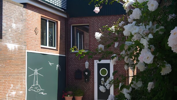 En byggnad av tegel med en grön dörr, krukväxter och vita blommor.