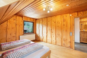 A wooden cabin room with a bed, a window, and a door leading to a kitchen.