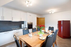 A modern kitchen with white cabinets, a wooden dining table, and a red refrigerator.