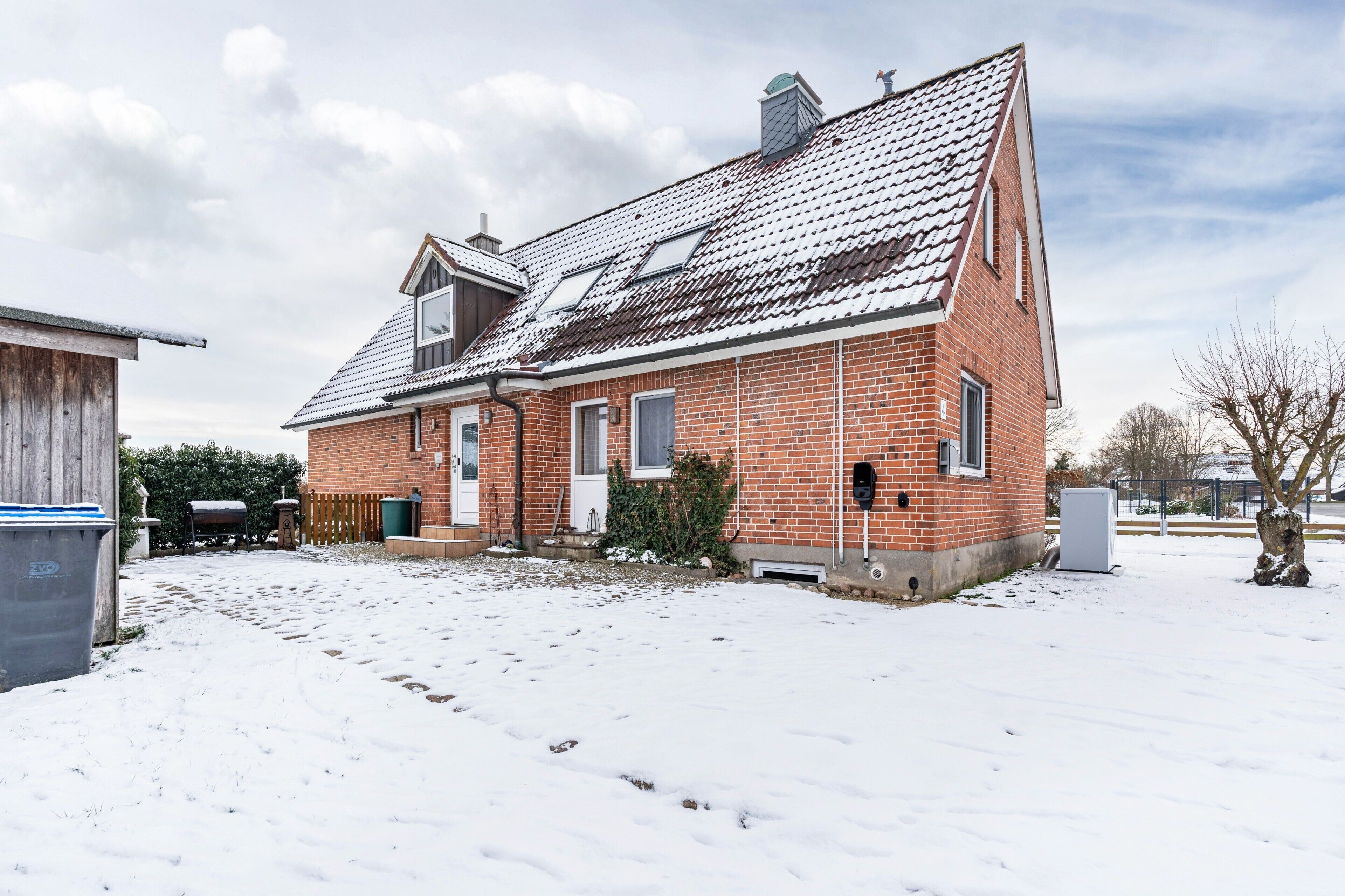 Une maison en briques avec un toit en pente, un petit porche et une cour enneigée.
