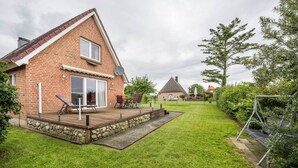 A brick house with a deck, a lawn, and a swing set. - Sustainable Holiday Apartment "Lichtblick" with Private Terrace, Garden, Wi-Fi & EV Charger (Grömitz)
