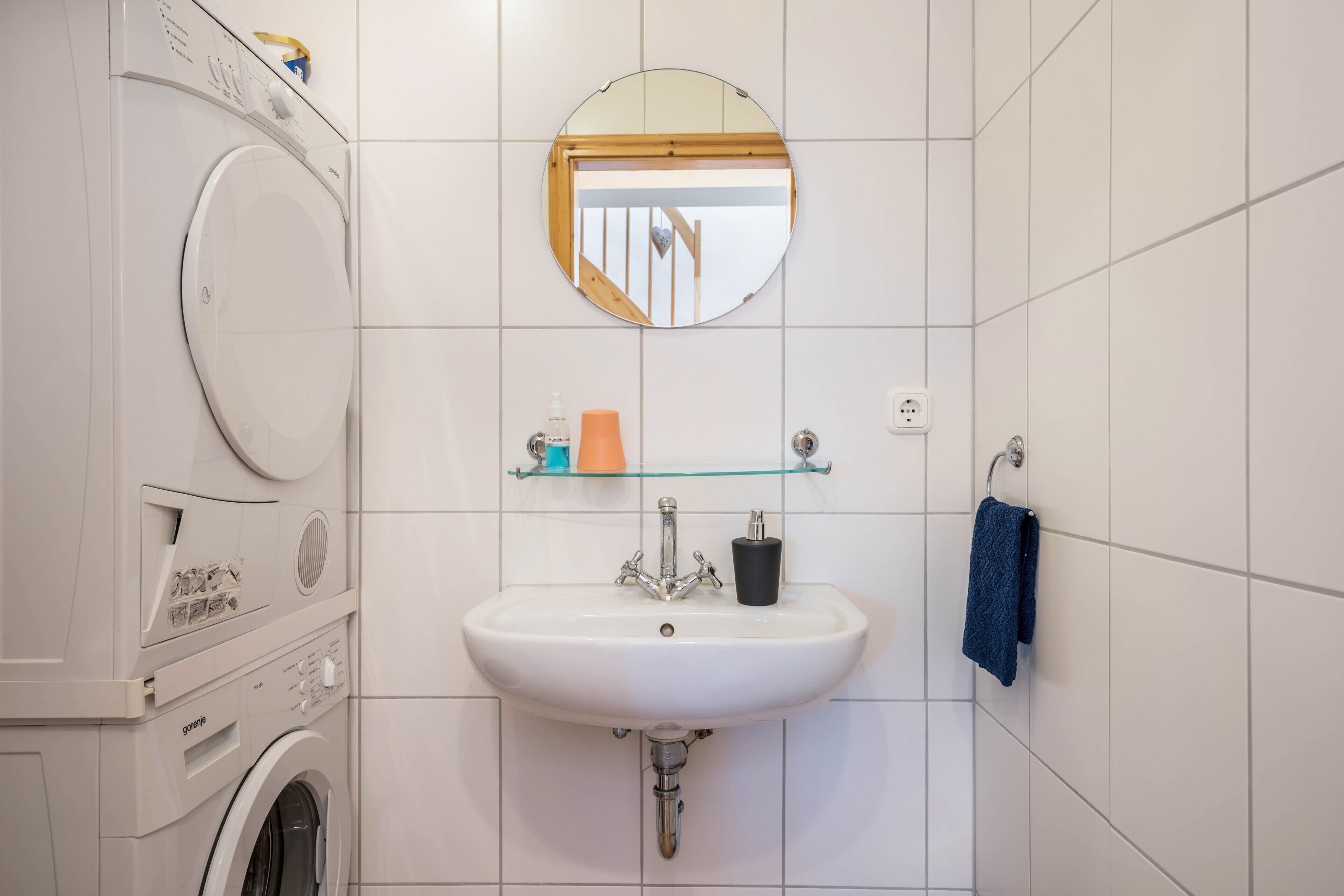 A bathroom with a washing machine, a sink, a mirror, and a towel rack.