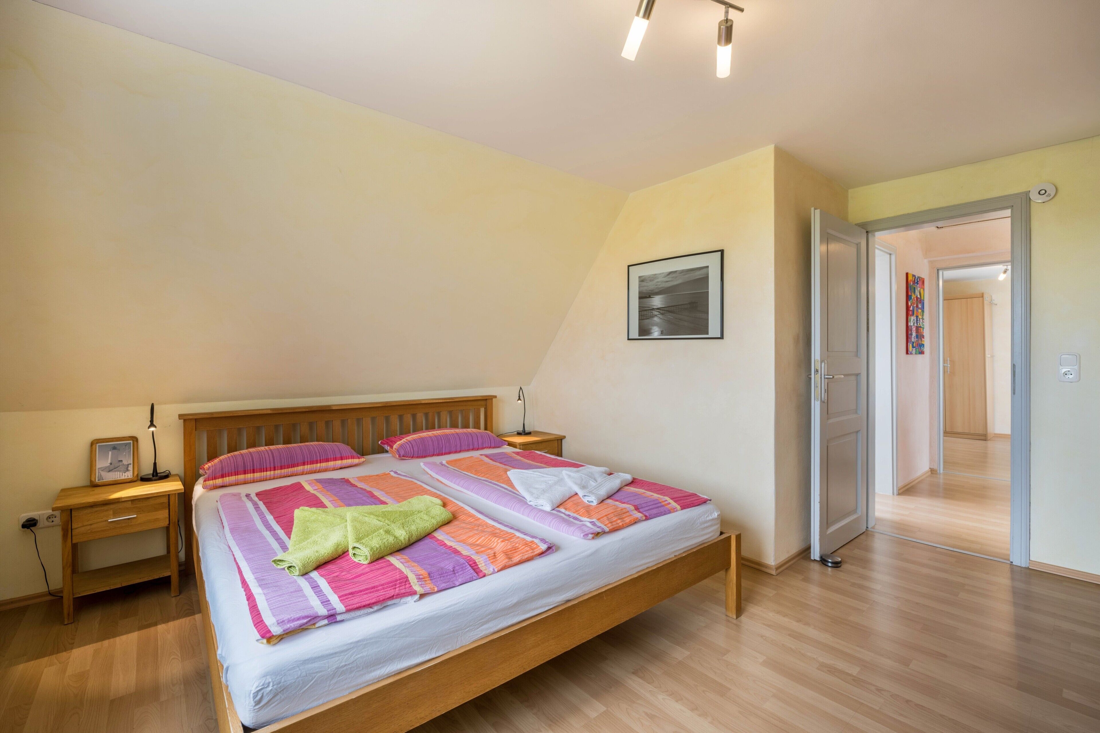 Ein Schlafzimmer mit einem hölzernen Bett, einem Nachttisch, einem Schreibtisch und einer Tür zu einem anderen Raum.