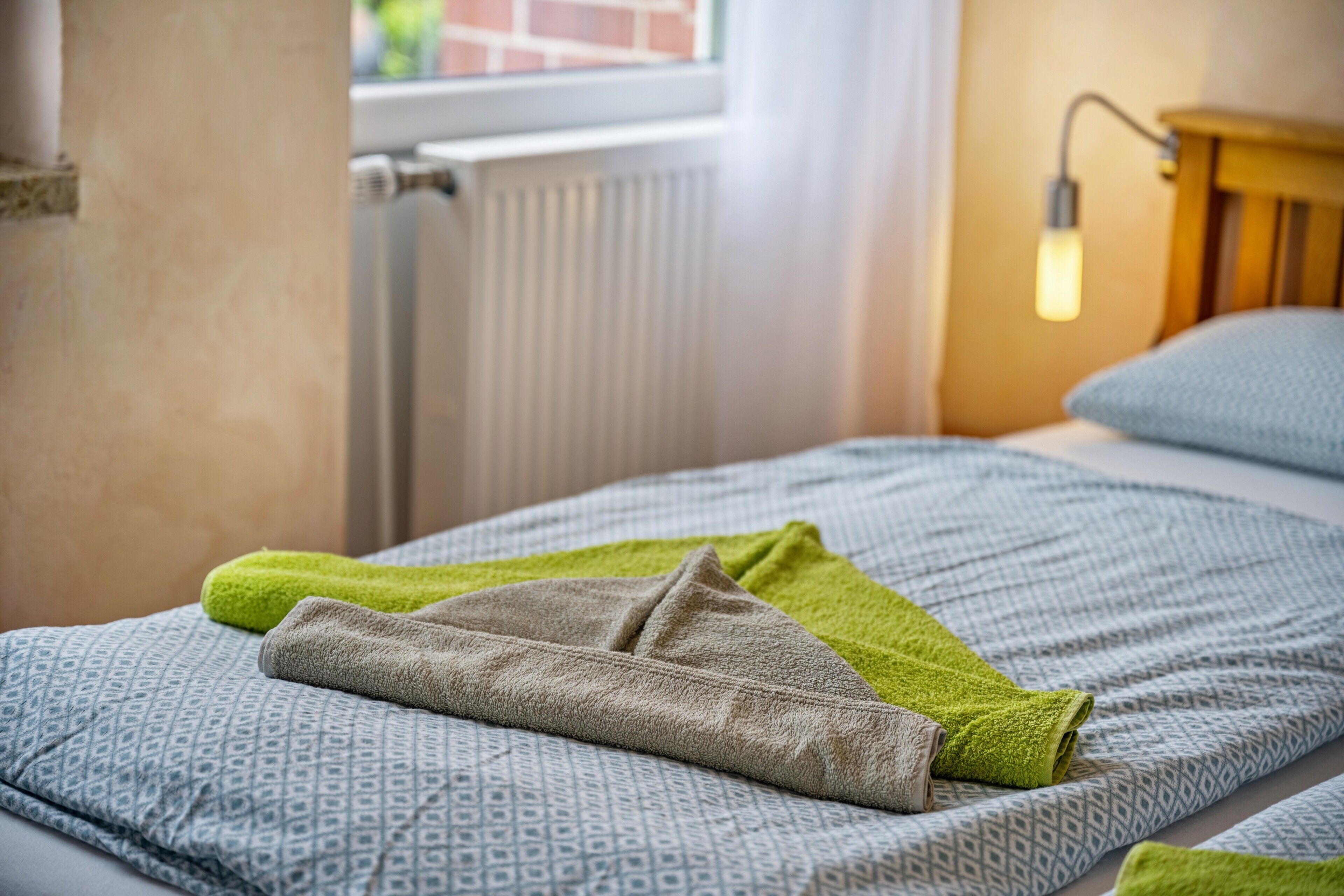 Un lit avec une literie à motifs, une serviette verte et une table de chevet en bois avec une lampe.