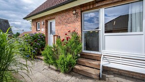 Une maison d’habitation avec une façade en briques, une porte d’entrée, une grande fenêtre et un banc en bois à l’extérieur.