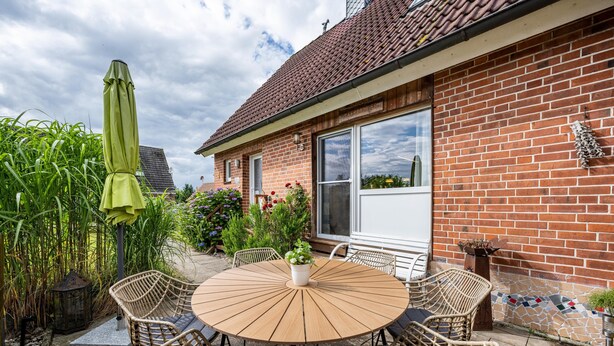 Une terrasse avec une table ronde, des chaises en osier et un parasol vert.