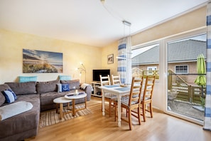 A living room with a sofa, a dining table with chairs, a TV, and a large window with a view of a house.