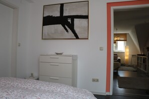 Un dormitorio con cama, cómoda, un cuadro y un umbral abierto que conduce a otra habitación.