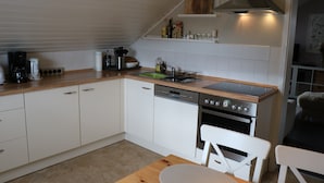 A modern kitchen with white cabinets, a wooden countertop, a dishwasher, an oven, and a dining area with a table and chairs. - Apartment 'Ferienwohnung Mandelblüte' with Mountain View and Wi-Fi (Schotten)