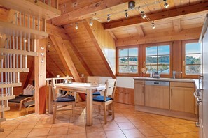 A wooden interior with a dining area, kitchen, and large windows offering a view.