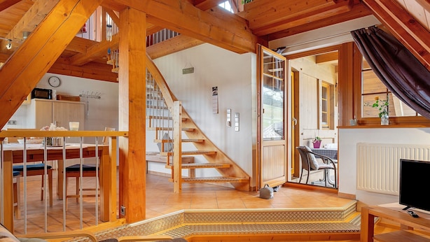 Un loft spacieux avec un escalier en bois, un coin repas, une cuisine et un salon équipé d’une télévision.