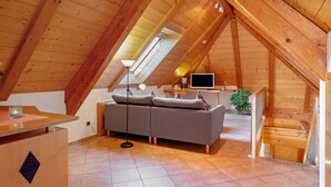 Une pièce mansardée chaleureuse avec un plafond en bois, un canapé, un bureau et une télévision.