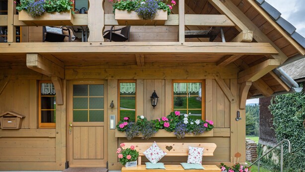Ein Holzhaus mit Haustür, Fenstern, einer Bank und Blumenkästen.