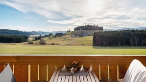Eine Holzterrasse mit Tisch und Stühlen, mit Blick auf eine grüne Landschaft mit Hügel und Bäumen.