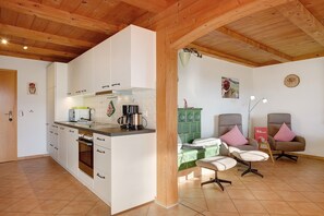 A kitchen with white cabinets, a coffee maker, and a green cabinet. There are two chairs with pillows and a small table.