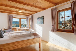 A wooden-framed room with a bed, a desk, and a window with curtains.