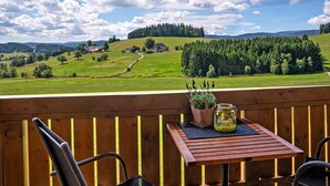 En træterrasse med et bord, stole og udsigt over et landligt landskab med huse og træer.