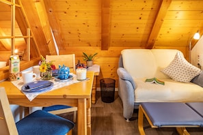 L’intérieur d’un chalet en bois chaleureux et accueillant, avec un coin repas, un canapé et une petite table sur laquelle se trouvent une tasse de café et une plante.