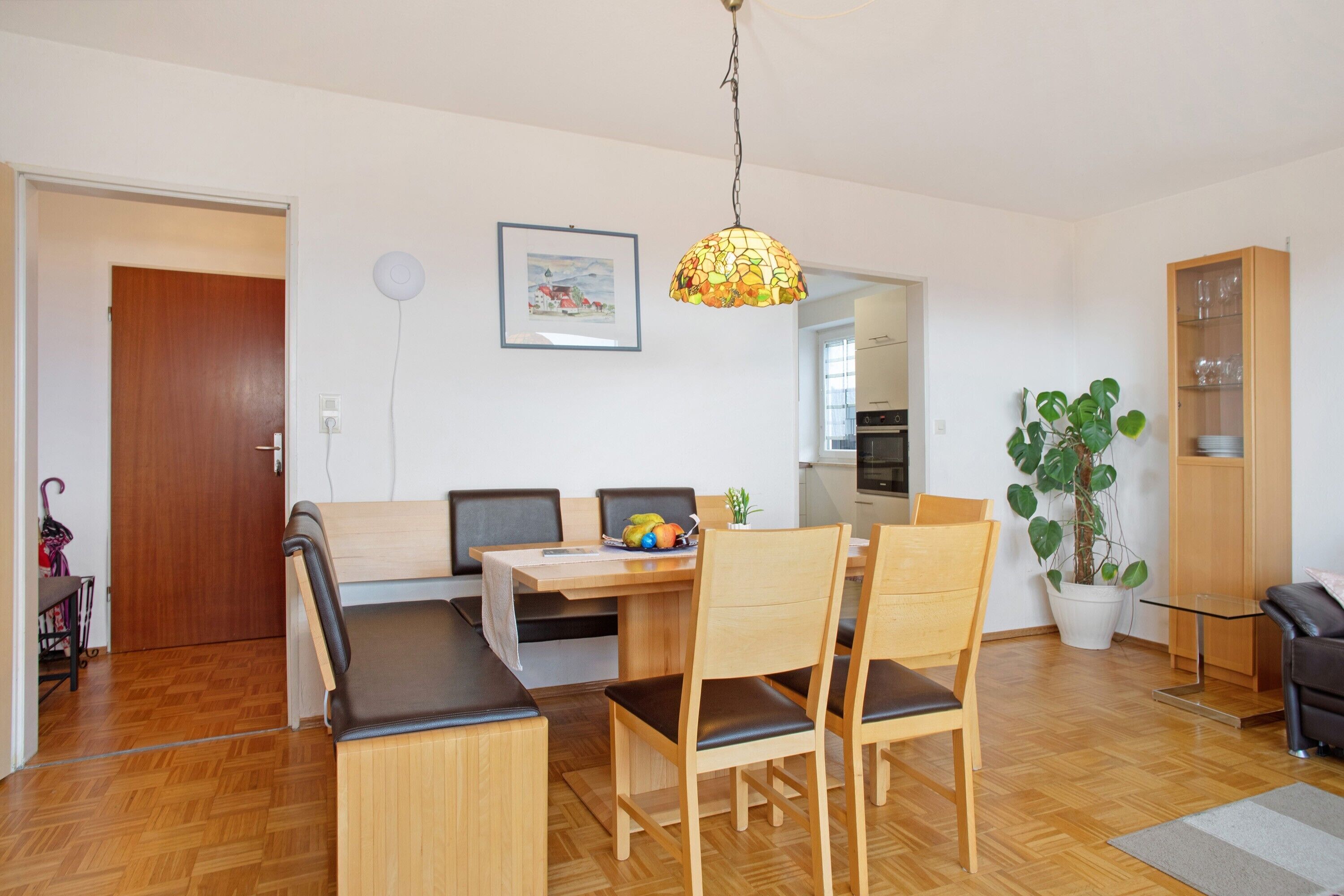 A dining area with a wooden table, chairs, a hanging light fixture, and a potted plant.