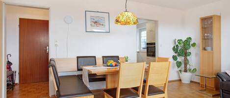 A dining area with a wooden table, chairs, a hanging light fixture, and a potted plant.