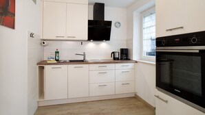 Una cucina moderna con mobili bianchi, una cappa aspirante nera, un forno Siemens e una finestra con persiane.