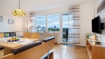 Ein modernes Wohnzimmer mit Essbereich, großen Fenstern, einem Fernseher und Blick ins Freie.