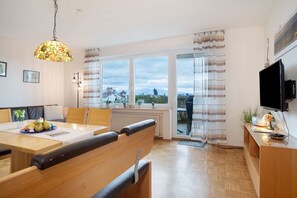 A modern living room with a dining area, large windows, a television, and a view of the outdoors.