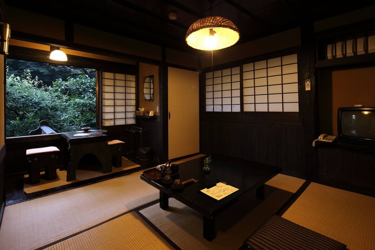 Una habitación tradicional japonesa con suelo de tatami, una mesa baja con una bandeja, una lámpara colgante y un televisor.