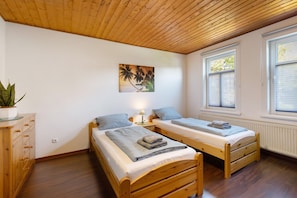 Een kamer met twee houten bedden, een houten kast, een potplant en een schilderij van palmbomen.