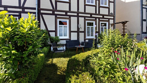 A traditional half-timbered building with a small patio area featuring outdoor seating and a garden. - Apartment '1 Obergeschoss' with Shared Terrace, Shared Garden and Wi-Fi (Ilsenburg (Harz))