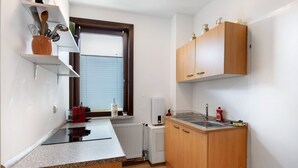 A compact kitchen with a built-in stove, a sink, wooden cabinets, and a window with blinds. - Apartment '1 Obergeschoss' with Shared Terrace, Shared Garden and Wi-Fi (Ilsenburg (Harz))