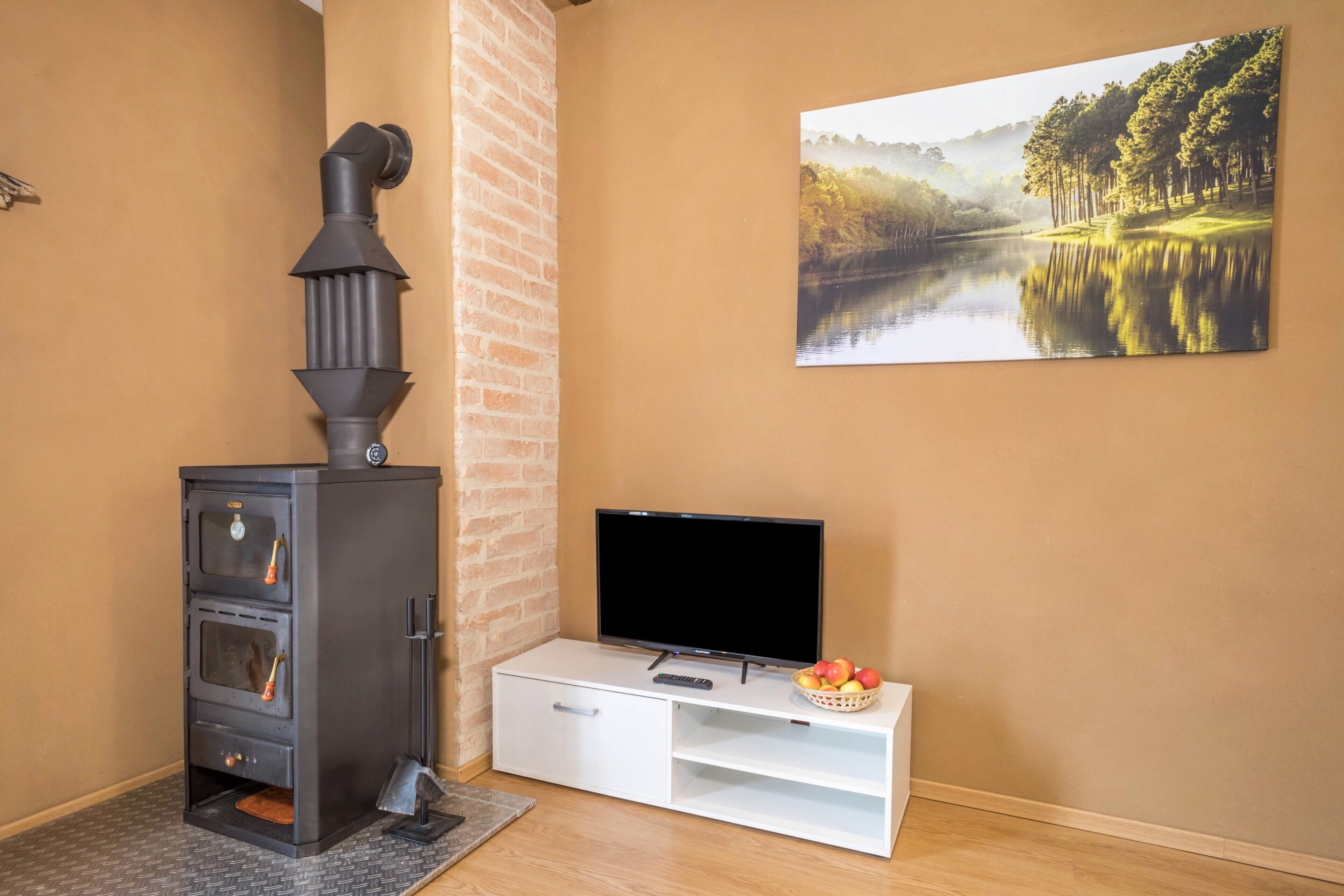 A room with a fireplace, a television, and a painting of a lake.