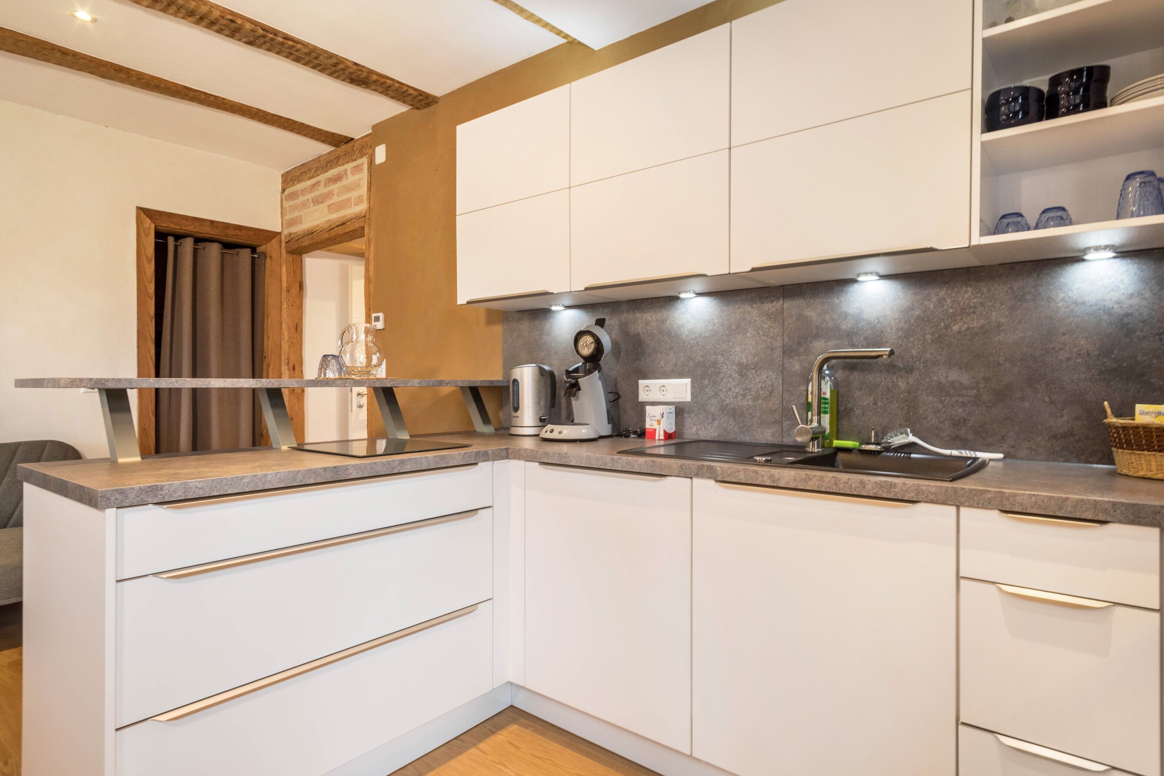 A modern kitchen with white cabinets, a granite countertop, a coffee maker, and a sink.