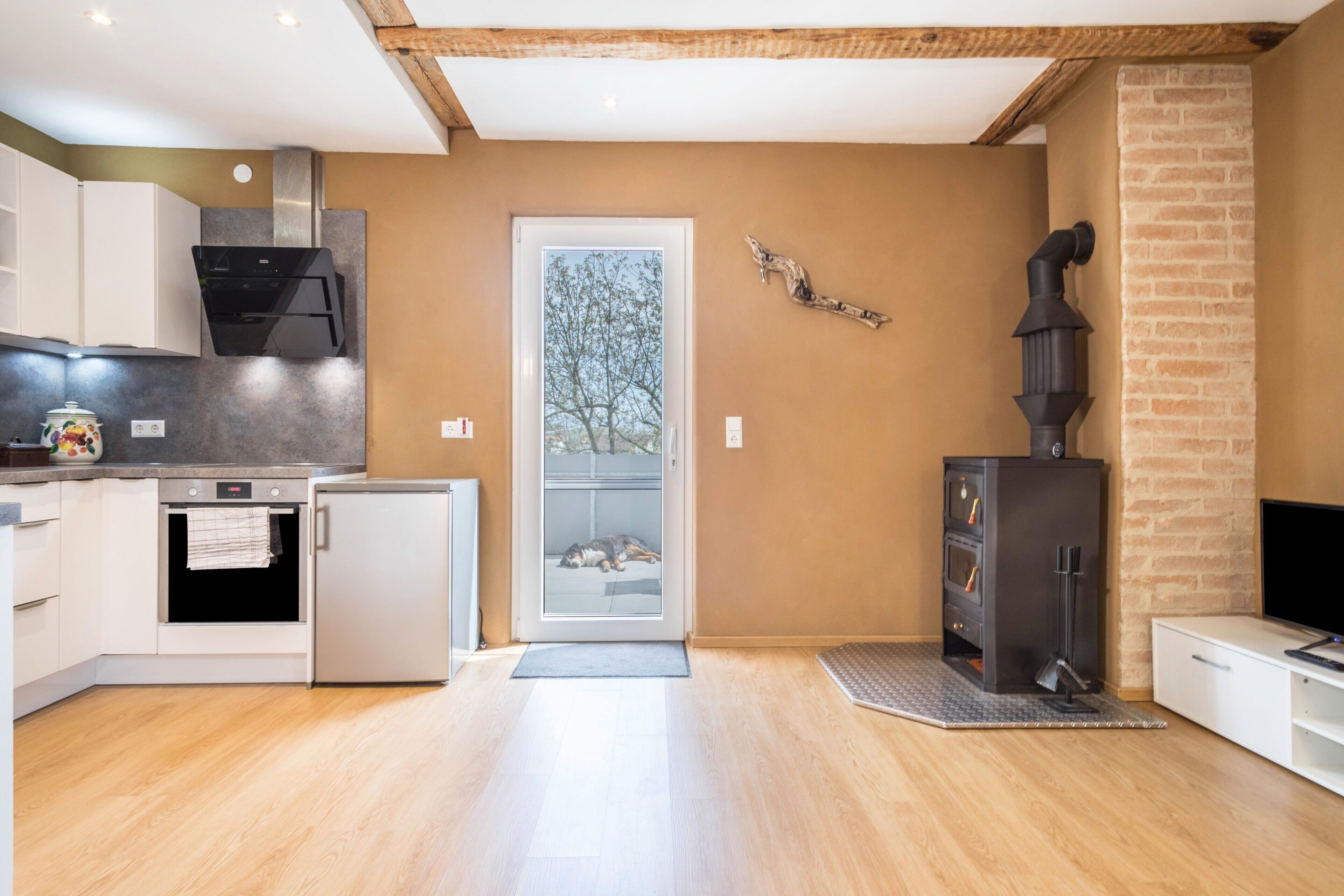 Eine moderne Küche mit Backofen, kleinem Kühlschrank und einem schwarzen Kaminofen.