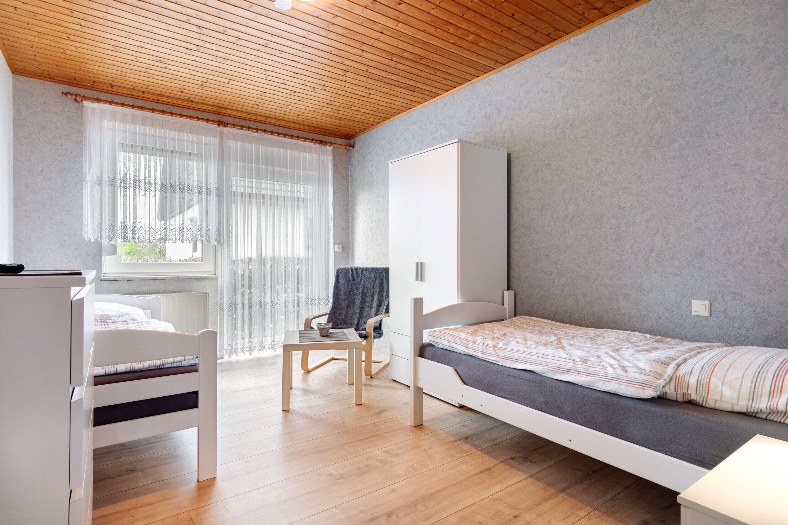 Una habitación pequeña con una cama, una silla, una mesa y un armario.