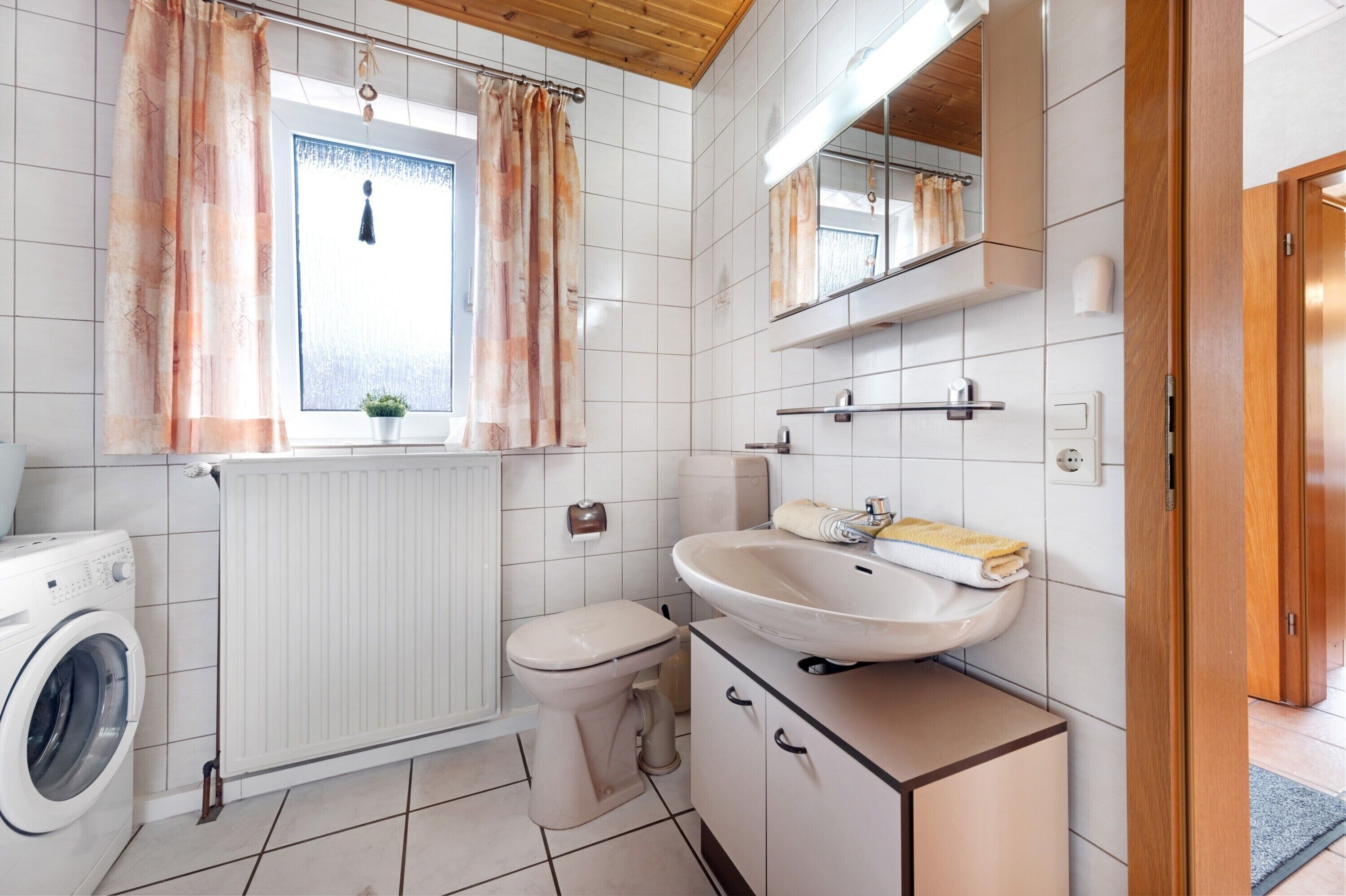 A bathroom with a washing machine, toilet, sink, and a window with curtains.
